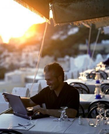Мъж, използващ лаптоп в кафене на открито по залез слънце