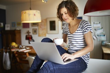 Portret van volwassen vrouw zittend op de keukentafel met behulp van laptop