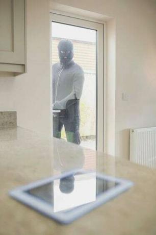 Ladrón mirando tablet pc a través de la puerta de la cocina