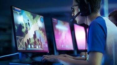 فريق من لاعبي الرياضات الإلكترونية المحترفين يلعبون في لعبة فيديو إستراتيجية MMORPG تنافسية في إحدى بطولات ألعاب الإنترنت. يتحدثون مع بعضهم البعض في الميكروفونات. الساحة تبدو رائعة مع أضواء النيون.