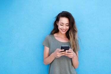青い背景に対して携帯電話を使用して若い笑顔の女性