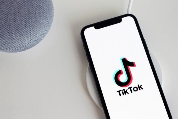 En smartphone och två andra enheter på ett vitt bord. Smarttelefonen har TikTok-logotypen på skärmen.