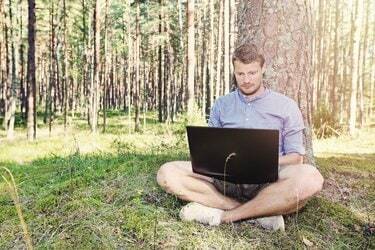 jaunuolis, dirbantis su savo nešiojamu kompiuteriu lauke