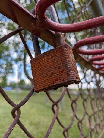 Una cerradura vieja y oxidada unida a una valla de tela metálica.