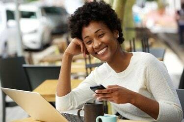 Mosolygó afrikai nő a kávézóban egy mobiltelefonnal