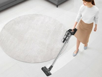 Wanita menyedot debu ruang tamu dengan Samsung Jet 75 Complete Cordless Stick Vacuum.