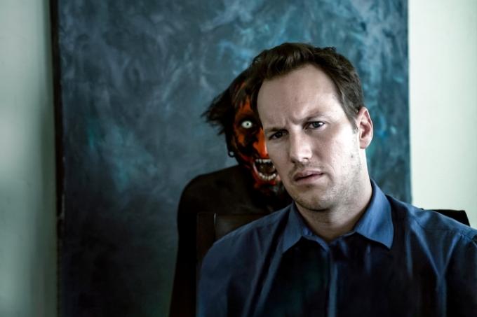 De hoofdpersoon van Insidious zit in een kamer naar voren te kijken terwijl een enge demon met een rood gezicht grommend achter hem verschijnt.