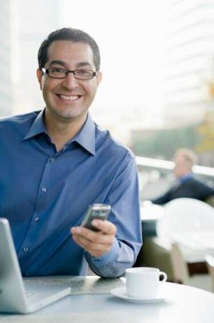 Smilende forretningsmann med telefon og datamaskin.