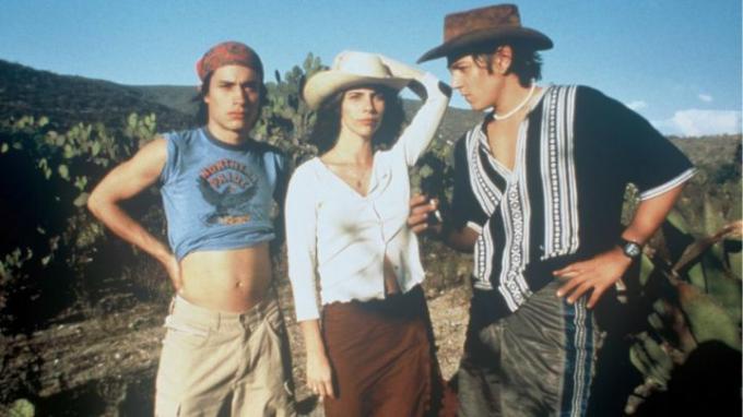 Twee jonge mannen en een vrouw staan ​​samen tegen een woestijnachtige achtergrond in de film Y Tu Mamá También uit 2001.