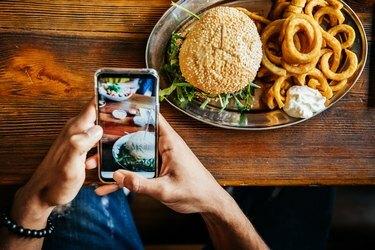 Man praten foto van hamburger met smartphone