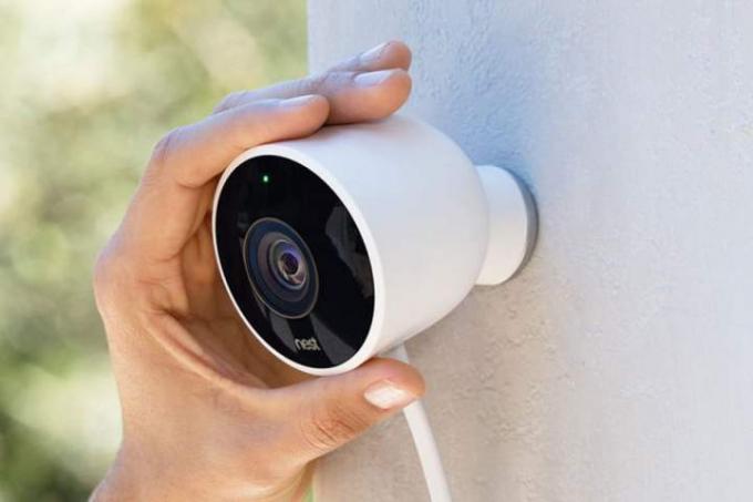 Et rede udendørs sikkerhedskamera, der placeres på et hjems sidevæg med hånden.