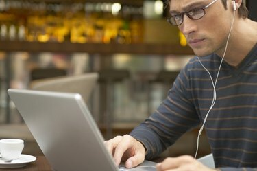 Čovjek sjedi za stolom u kafiću koristeći laptop i slušalice