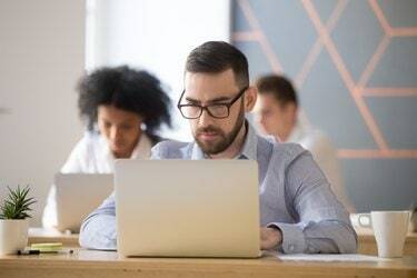 Ernster Geschäftsmann, der sich auf Computer-Online-Arbeit im Coworking-Büro konzentriert