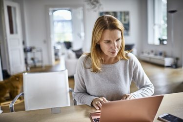 امرأة تستخدم الكمبيوتر المحمول على الطاولة في المنزل