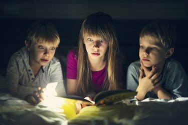 Niños leyendo un libro con historias de miedo por la noche.