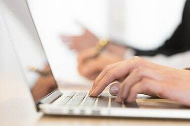 Žena koristi laptop u uredu tijekom sastanka. Ruke u krupnom planu