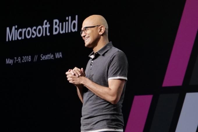 Satya Nadella, PDG de Microsoft, debout sur scène dans une pose accueillante.