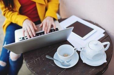 Moters rankos su nešiojamojo kompiuterio planšete ir arbata lauke kavinėje
