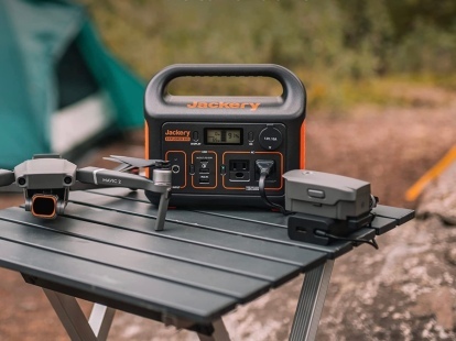 Jackery Portable Power Station Explorer 300 steht auf einem Tisch auf einem Campingplatz neben einer Drohne.