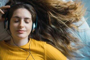 Potret wanita muda tersenyum berbaring di tempat tidur mendengarkan musik dengan headphone