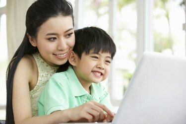 Čínska matka a syn sedia pri stole a používajú laptop doma