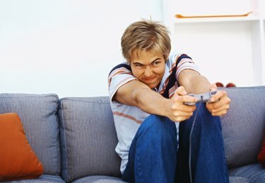 ソファに座ってコンピューターゲームをプレイしている若い男の正面図