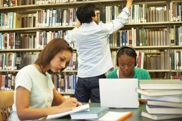 To kvinnelige studenter som studerer på biblioteket, mannlig student i bakgrunnen