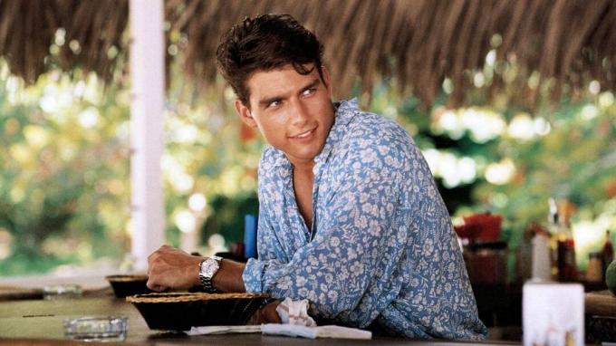 Tom Cruise sebagai Brian Flanagan duduk di bar pantai dalam film Cocktail.