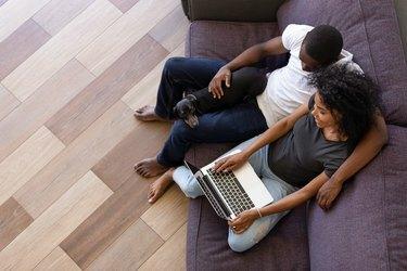 Šťastný africký pár pomocí počítače sedí na pohovce s domácím mazlíčkem