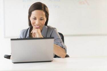 Femeie de afaceri cu mâna pe bărbie folosind laptopul la birou