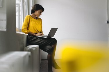 Kvinna som sitter vid fönstret med bärbar dator