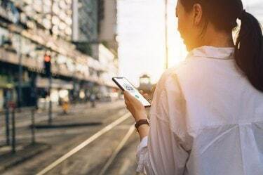 Mlada žena koja koristi mobilnu aplikaciju na pametnom telefonu za organiziranje prijevoza u gradskoj ulici u zalazak sunca