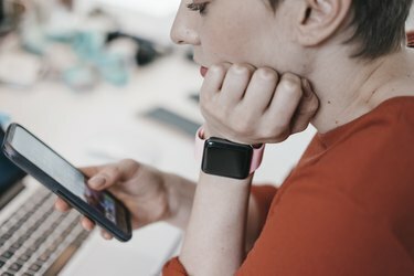 Frau trägt Smartwatch mit Handy am Schreibtisch im Büro