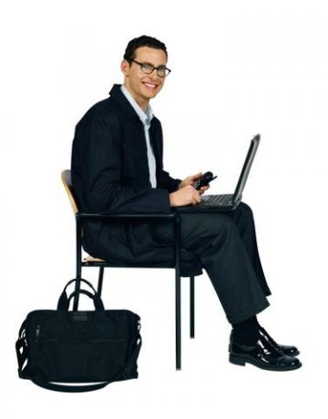 Uzņēmējs sēž uz krēsla ar klēpjdatoru un mobilo tālruni