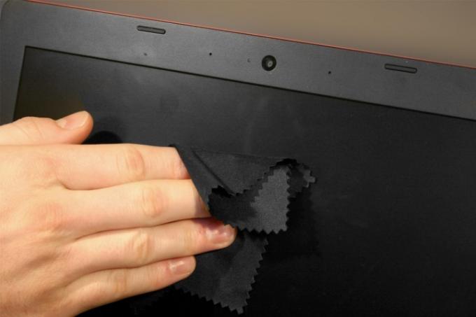 Рука человека чистит экран ноутбука тканью из микрофибры.