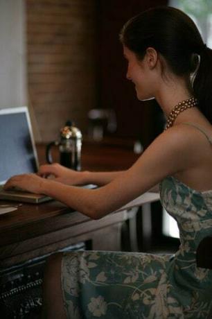 Jauna moteris naudoja nešiojamąjį kompiuterį bare kavinėje.