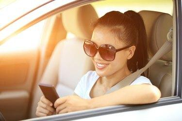 šťastná žena řidič používá svůj mobilní telefon v autě