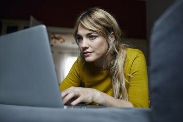 Retrato de mulher deitada no sofá em casa usando um laptop