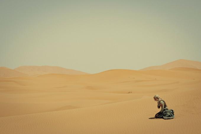 Uma mulher sentada em um vasto deserto na terceira temporada de The Witcher.