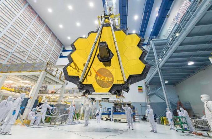 NASA 기술자들이 크레인을 사용하여 제임스 웹 망원경을 들어올려 메릴랜드주 그린벨트에 있는 NASA 고다드 우주비행센터의 클린룸으로 옮기고 있습니다. 
