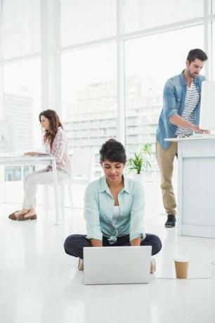 Mulher de negócios casual sentada no chão usando um laptop