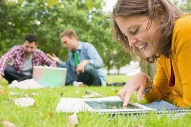 Siswa menggunakan tablet PC sementara laki-laki menggunakan laptop di taman
