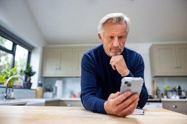 Idősebb férfi otthon egy mobilalkalmazás segítségével a mobiltelefonján
