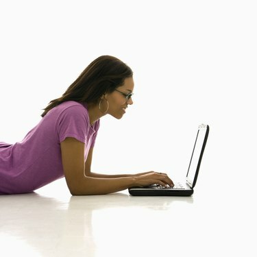 Bočný pohľad na afroamerickú stredne dospelú ženu ležiacu na podlahe pomocou prenosného počítača.