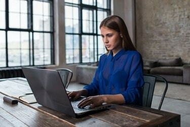 Destul de tânără brunetă care lucrează pe laptop la o masă de lemn într-un studio spațios, întunecat