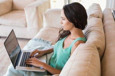 امرأة سمراء جميلة تستخدم الكمبيوتر المحمول الخاص بها على الأريكة