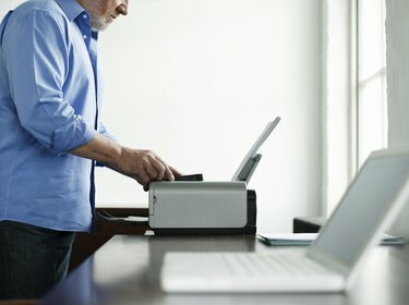 Vyras namuose naudoja spausdintuvą prie studijų stalo