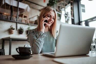 Mulher jovem elegante falando ao telefone e usando o laptop. Visão de baixo ângulo.