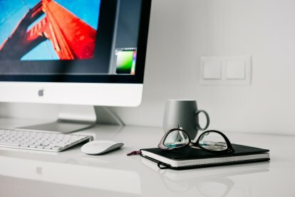 iMac på et skrivebord med briller og en notatbok fra Pixabay.