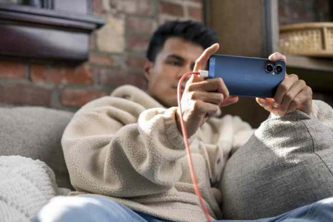 Mann entspannt sich, während er das an das Ladekabel angeschlossene OnePlus Nord N20-Telefon in der Hand hält.